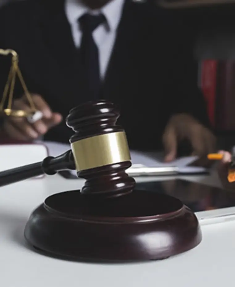 A wooden gavel resting on a table, with scales of justice and legal documents in the background, suggesting a courtroom setting